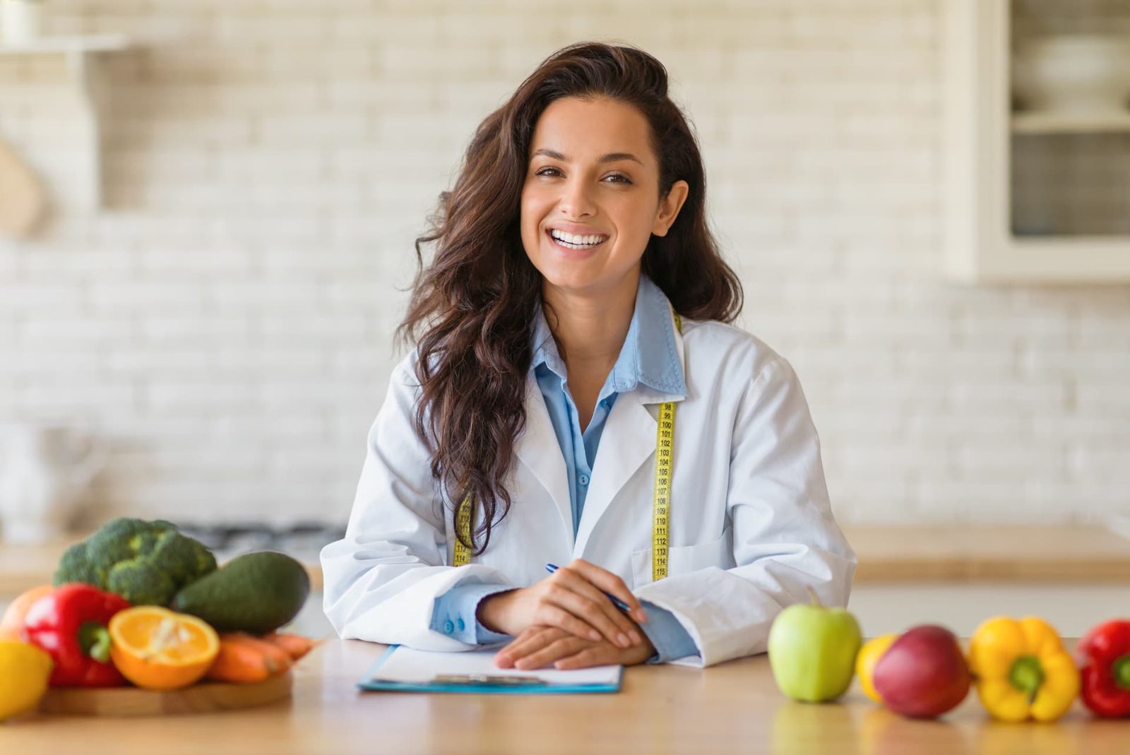 Nutricionista da Clínica Higya sorrindo à mesa com frutas e legumes e a ficha do plano alimentar